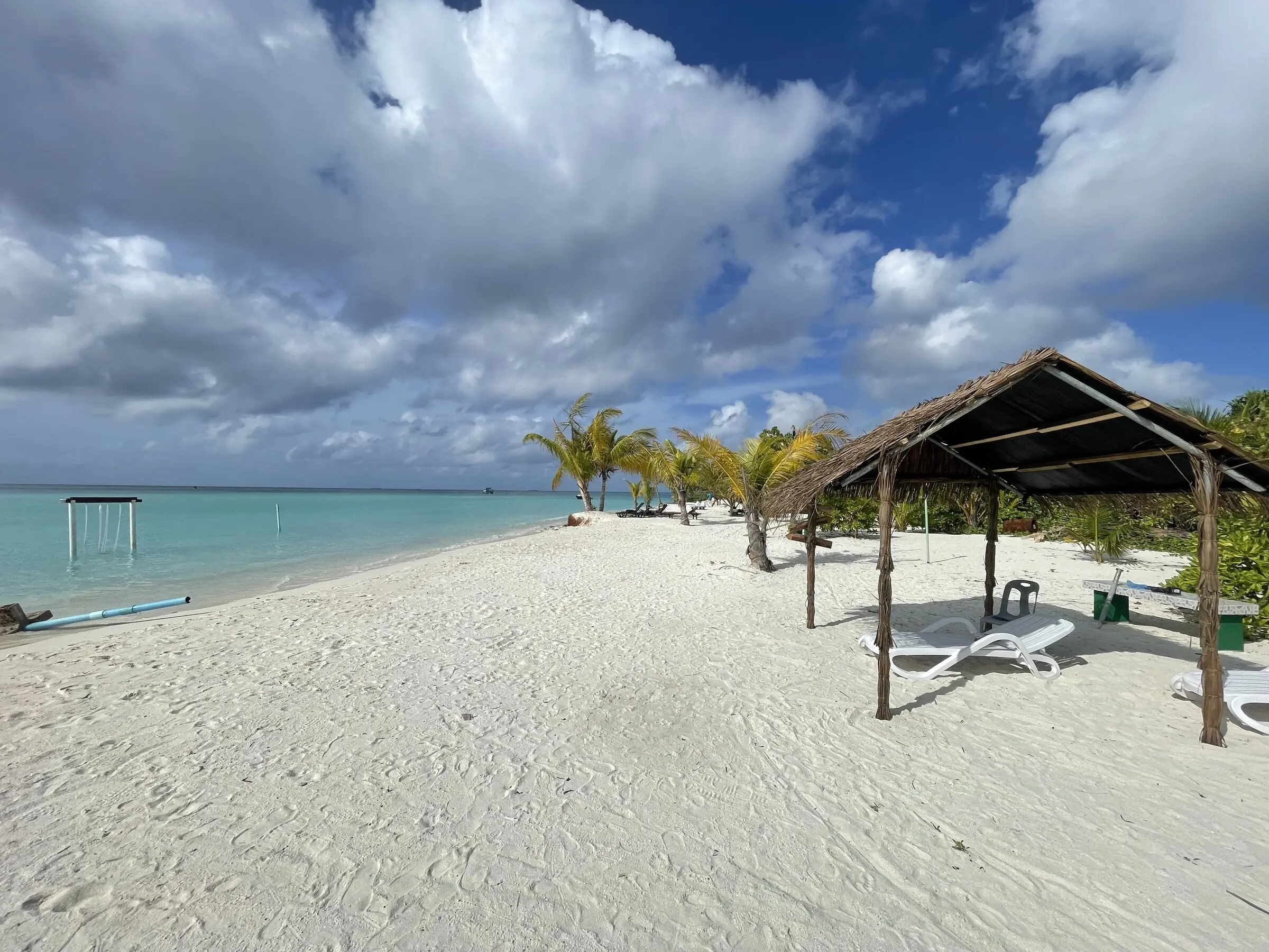 Shaded cabana on a quiet stretch of Maamigili beach beside calm turquoise water